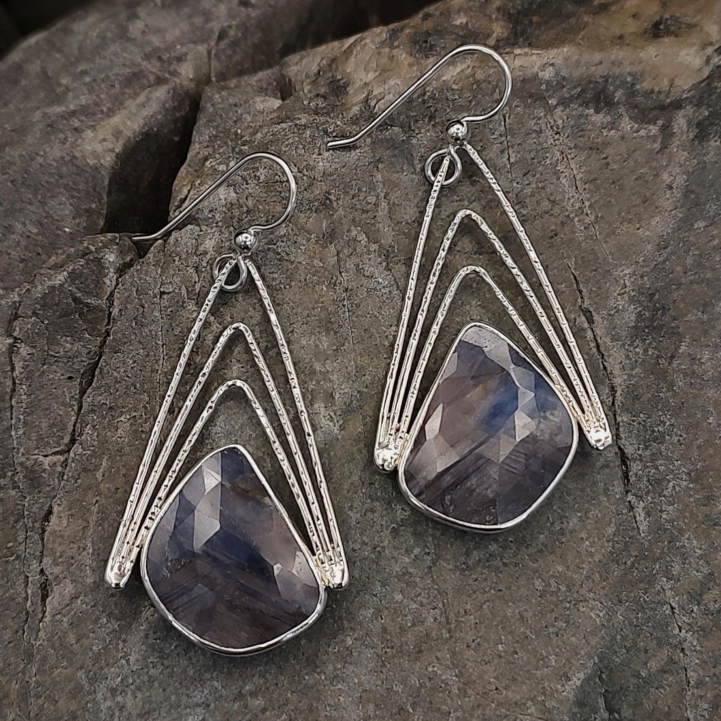 Silver earrings with faceted stones on a stone surface